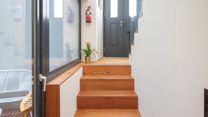 A wooden staircase leading to a dark door, a potted plant, and a fire extinguisher on the wall.