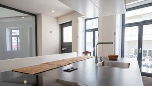 A modern kitchen with a large island, a sink, and a window overlooking a balcony.
