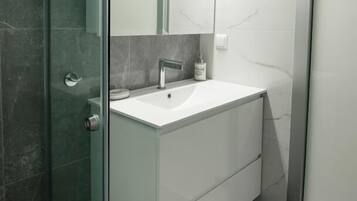 A modern bathroom with a glass shower enclosure, a white sink, and a large mirror.