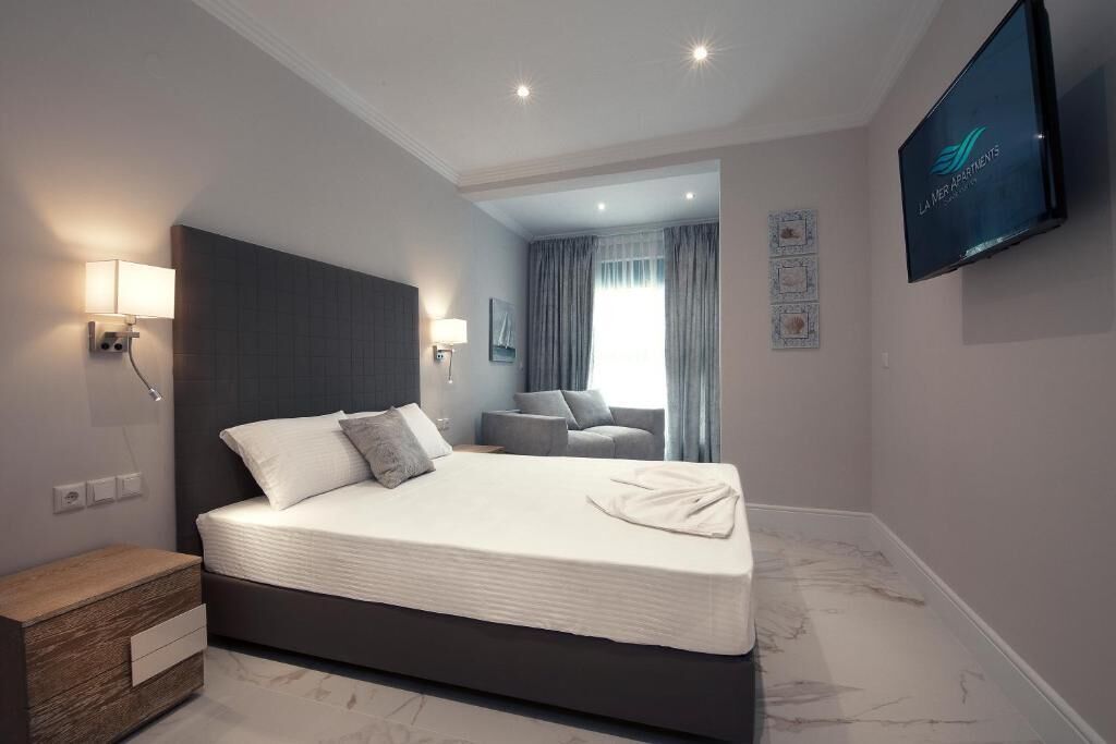 A modern hotel room with a large bed, bedside lamps, a flat-screen TV, and a view of the living area.