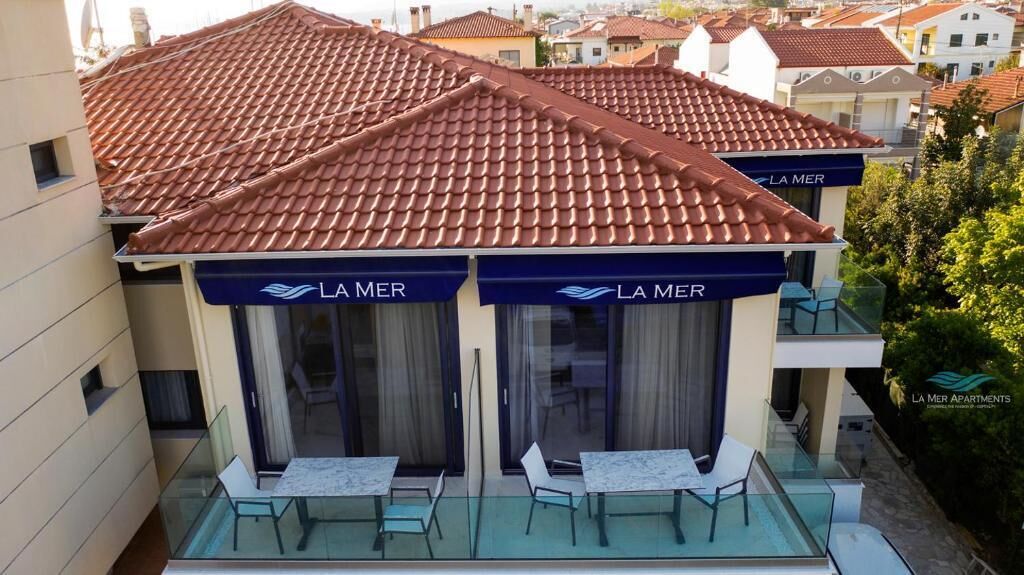 Um hotel com telhado de telhas vermelhas, duas varandas com guarda-corpos de vidro e a inscrição 'LA MER' nas marquises.
