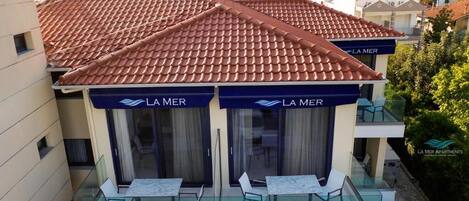 Un hotel con techo de tejas rojas, dos balcones con barandillas de vidrio y el nombre 'LA MER' en los toldos.