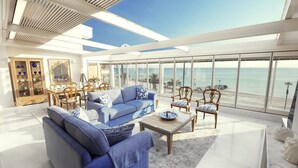 Un salón amplio con un gran ventanal con vistas a la playa, un aparador de madera con puertas de cristal y un comedor con mesa y sillas.