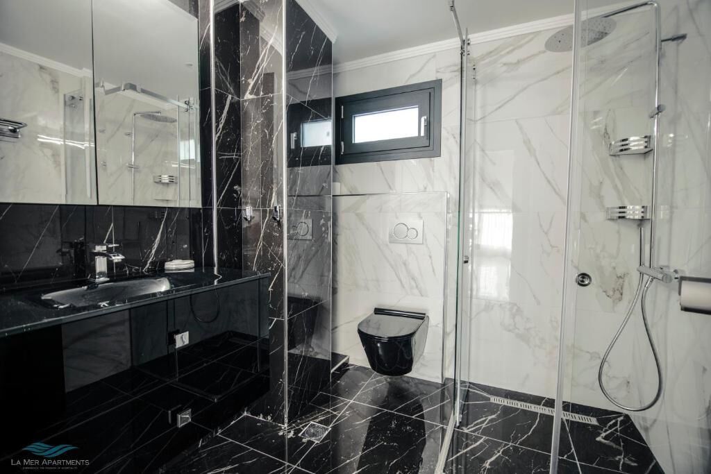 A modern bathroom with a glass shower enclosure, a black marble vanity, and a large mirror.