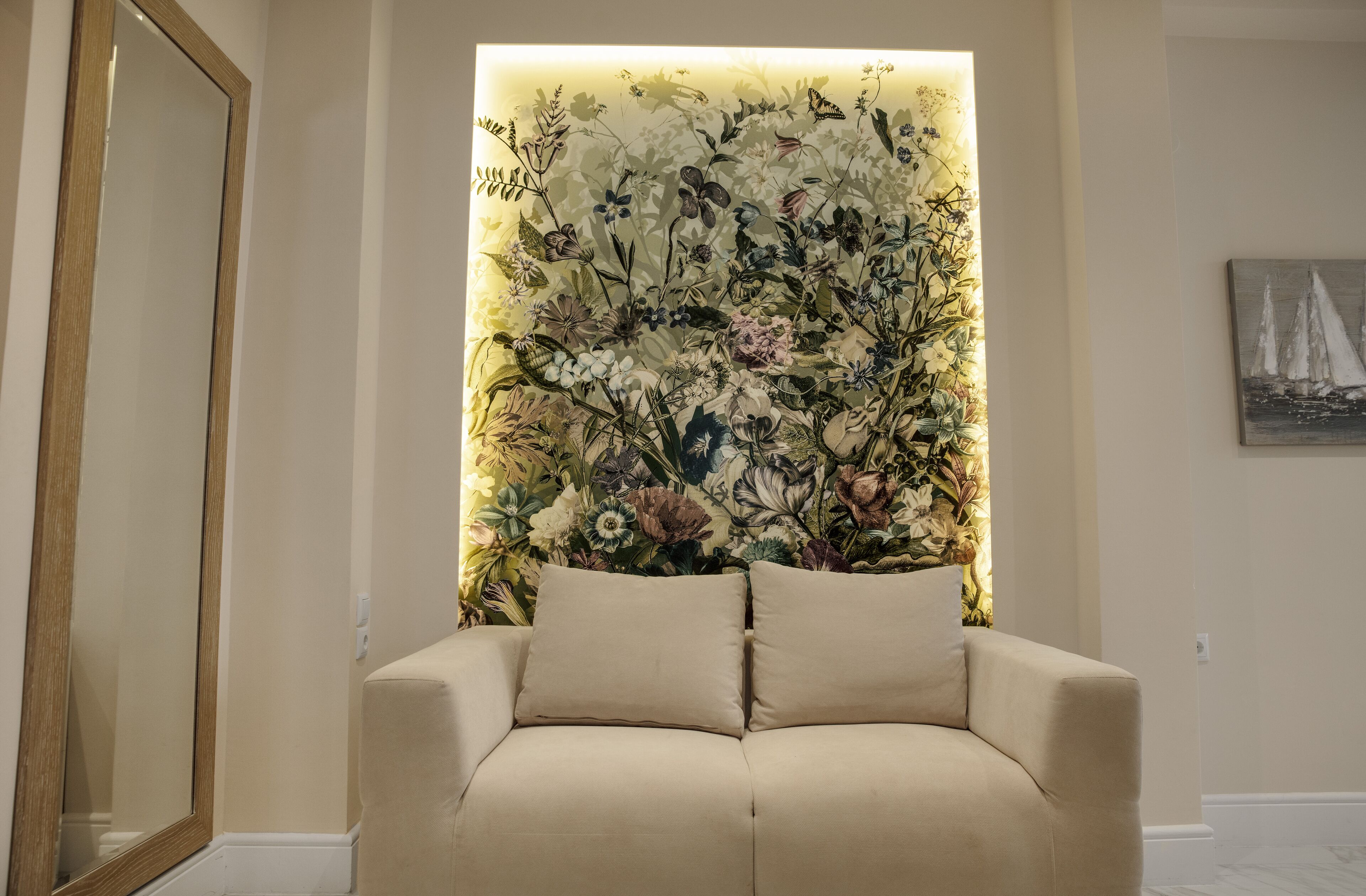 A room with a beige sofa, a floral wall art piece, and a framed picture on the wall.