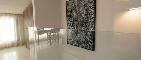 A modern interior with a glass railing, a dining table, and a large black and white floral artwork on the wall.