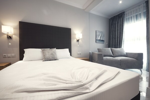 A modern hotel room with a large bed, two bedside lamps, a grey sofa, and a window with curtains.