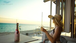 Una persona sentada a una mesa con una botella de champán y una copa, con vistas a una playa.