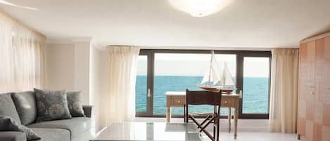 Un salon moderne avec un canapé, une table à manger et une vue sur la mer grâce à de grandes fenêtres.