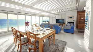 Una sala de estar moderna con comedor, ventanas amplias y vista al mar.