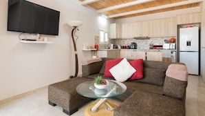 A modern living room with a glass coffee table, a sofa with red and white cushions, and a flat-screen TV mounted on the wall. - Sweet Cottage Retreat (Zakynthos)
