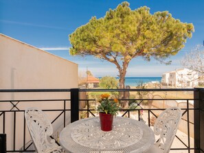 A balcony with a round table, two chairs, a potted plant, and a view of the sea and buildings. - Sweet Cottage Retreat (Zakynthos)