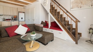 A modern living room with a glass coffee table, a sofa with red and white cushions, a staircase with wooden steps, and a kitchen in the background. - Sweet Cottage Retreat (Zakynthos)