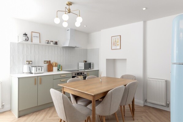 A modern kitchen with a dining area, white cabinetry, a wooden table, and a unique ceiling light fixture. - 💫 Chic 2-Bed Apartment in Historic Guest House | Central Rothbury Retreat (Rothbury)
