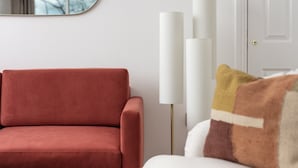 Ein rotes Sofa, ein weißer Sessel und eine hohe, weiße Stehlampe in einem Raum mit einer weißen Tür und einem Spiegel an der Wand.