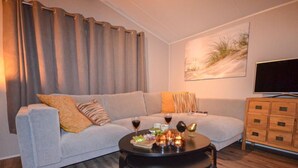 A modern living room with a grey sofa, a round coffee table with candles, and a television on the wall.