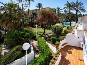 Um jardim ajardinado com palmeiras, uma piscina e um edifício com varandas.