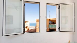 Een kamer met drie ramen, elk met uitzicht op een gebouw met een balkon en een heldere lucht.
