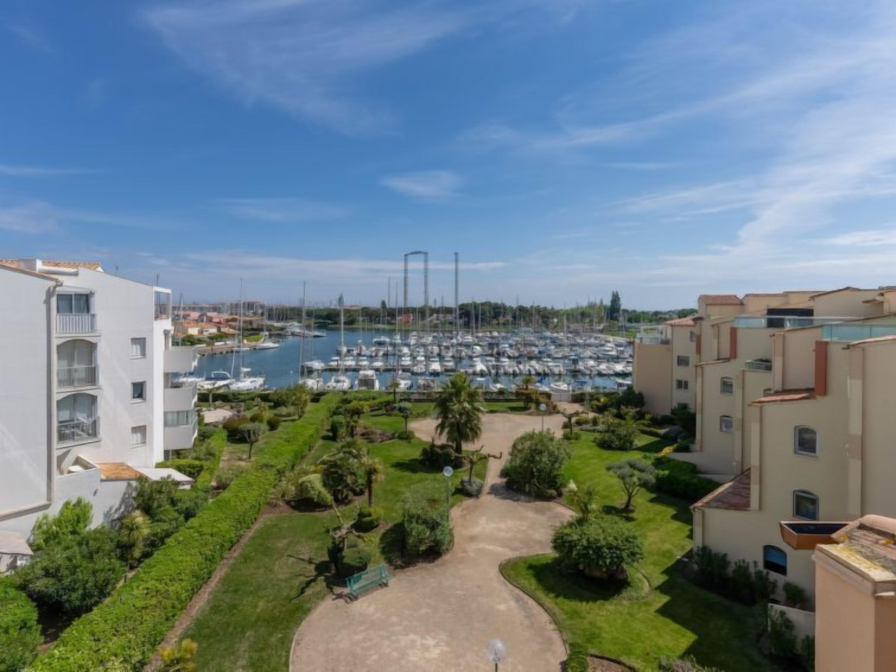 A marina with boats, surrounded by residential buildings with balconies and a well-maintained garden.