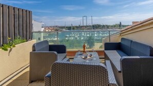 Eine Dachterrasse mit Korbmöbeln, einem Tisch mit Gläsern und einer Flasche sowie Blick auf einen Yachthafen mit Booten.