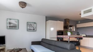 A modern living room with a grey sofa, a TV, and a coffee table. There is a kitchen in the background with a dining table and chairs. - Apartment Maïlys by Interhome (Arcachon)