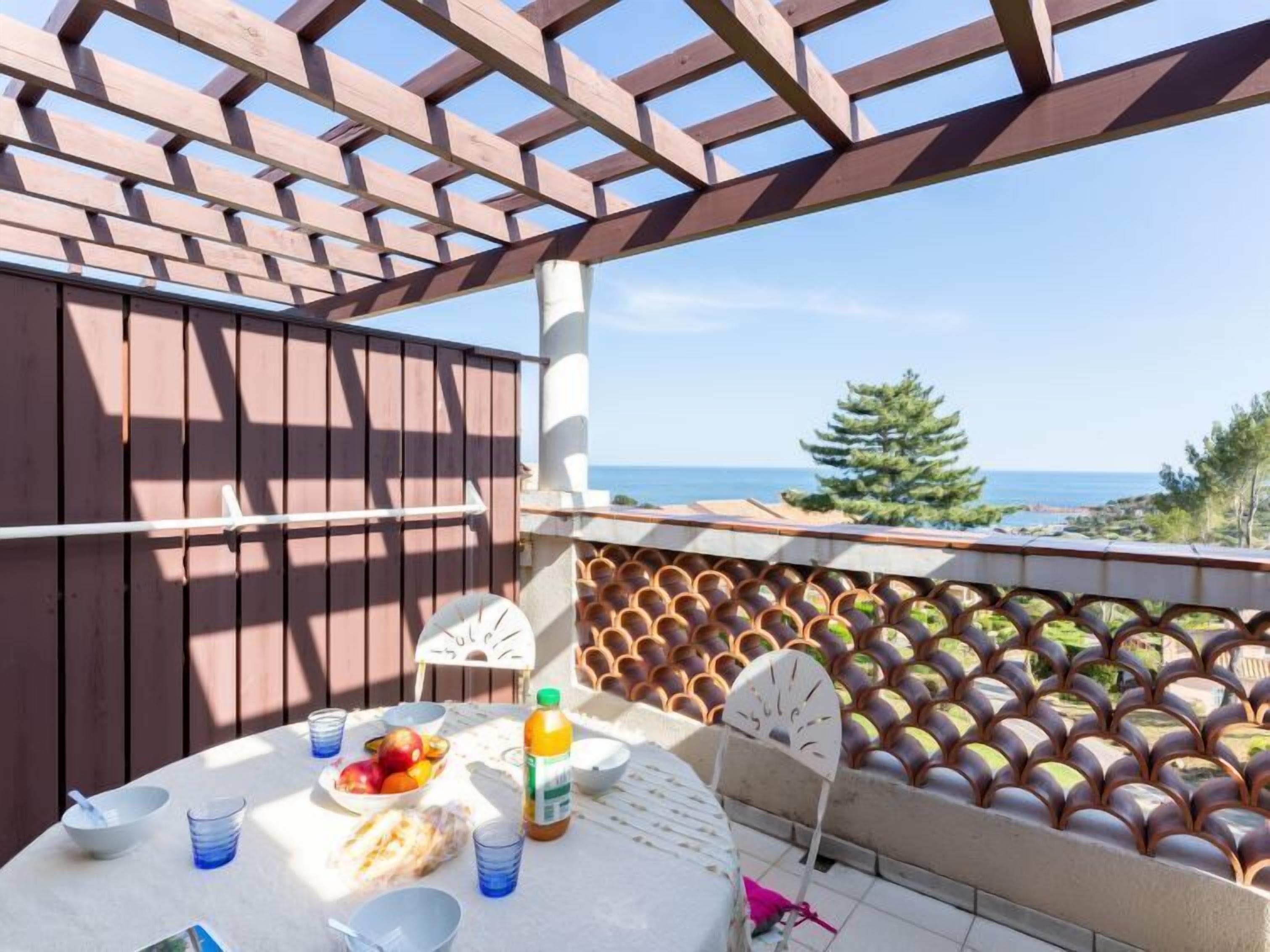 Une terrasse agrémentée d’une pergola en bois, une table garnie de nourriture et de boissons, et une vue sur la mer.