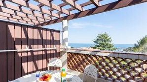 Una terraza con una pérgola de madera, una mesa con comida y bebidas, y vistas al mar.