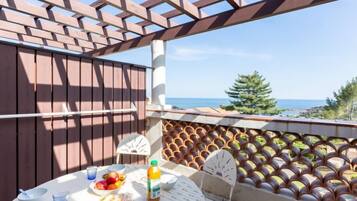 Una terraza con una pérgola de madera, una mesa con comida y bebidas, y vistas al mar.