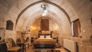 Un dormitorio rústico con techo abovedado de piedra, cama de madera, alfombra estampada y una pequeña mesa con sillas.