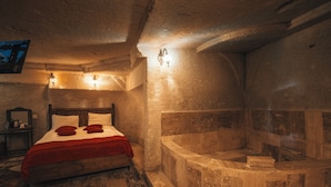 Una habitación con una cama de madera, una bañera de piedra y una pared de piedra.