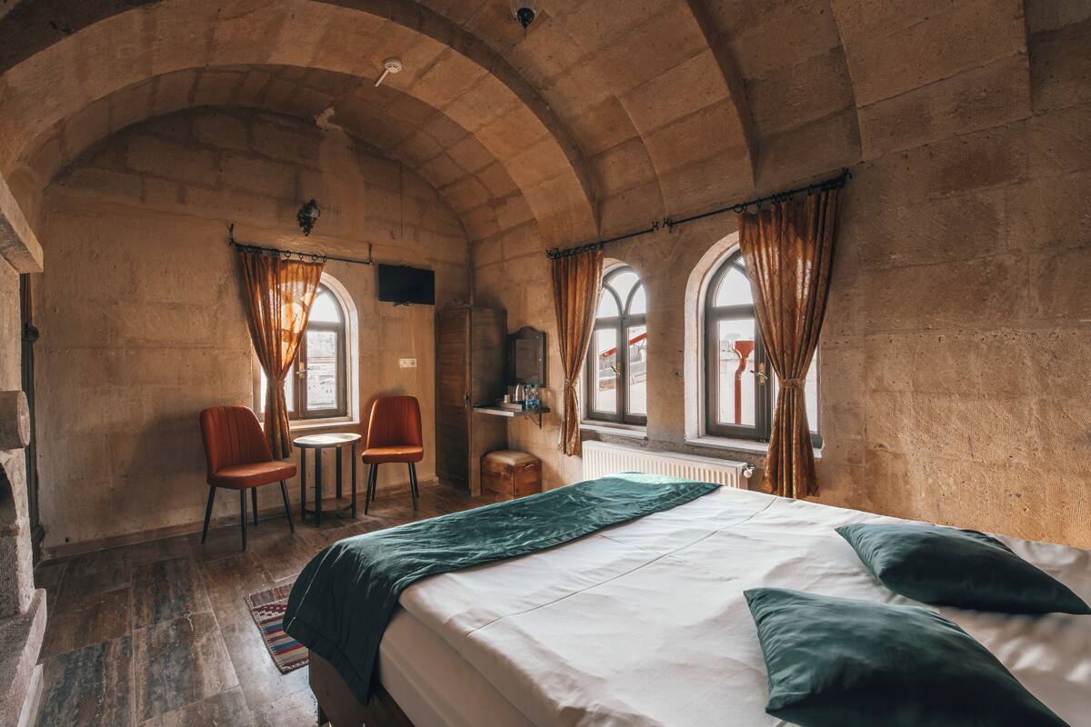 A room with a bed, a chair, a small table, and a window with curtains.