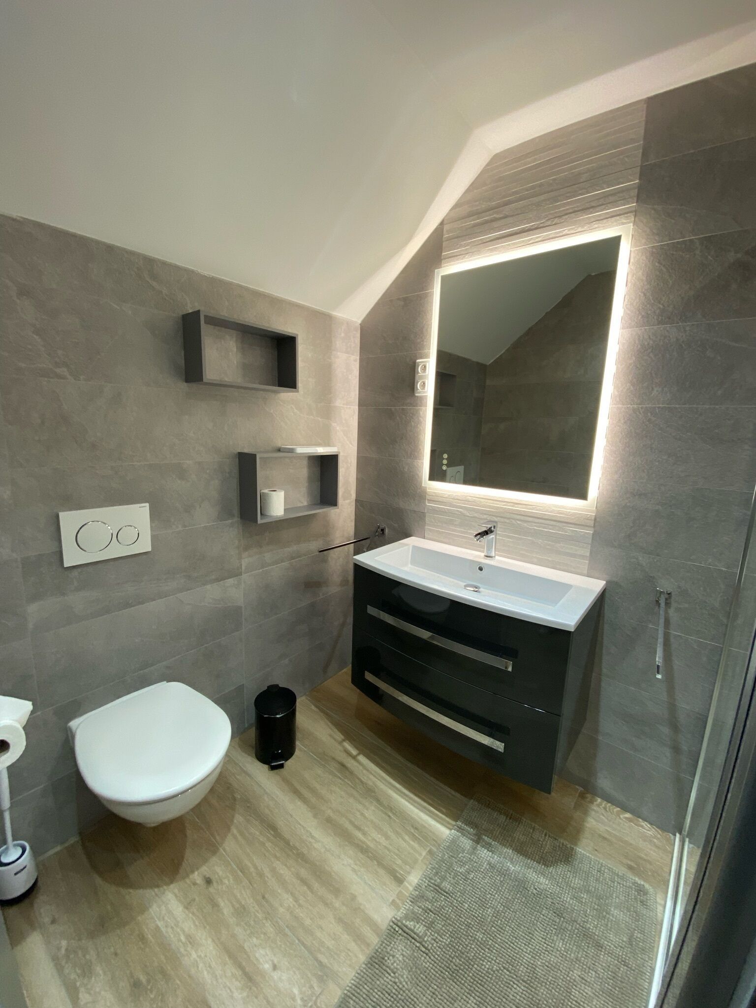 A modern bathroom with a white toilet, a black vanity with a mirror, and a shower area.