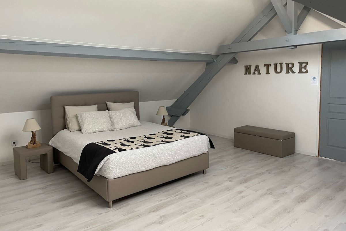A bedroom with a bed, bedside tables, a bench, and a wall with the word "NATURE".