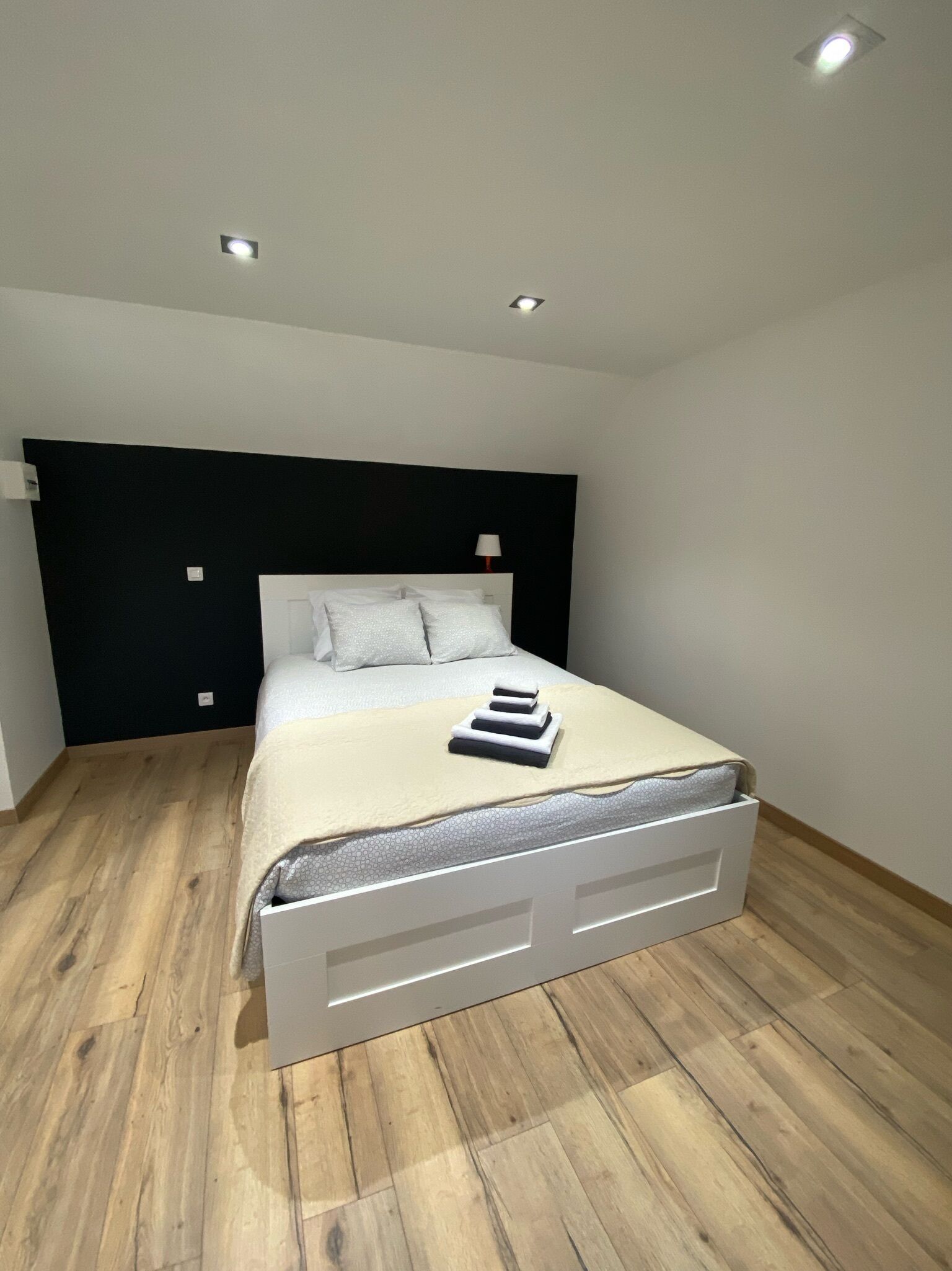 A modern bedroom with a bed, wooden flooring, a black headboard, and recessed ceiling lights.