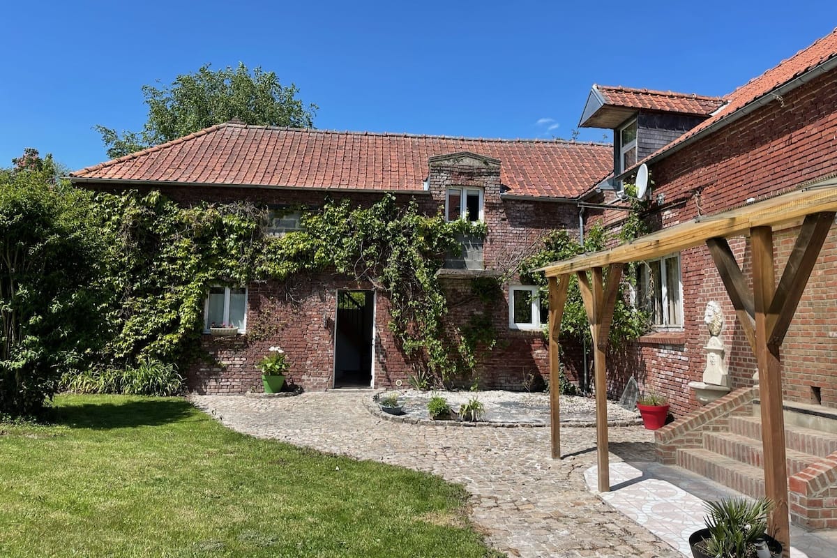 A brick house with a tiled roof, a stone pathway, and a garden area with potted plants.