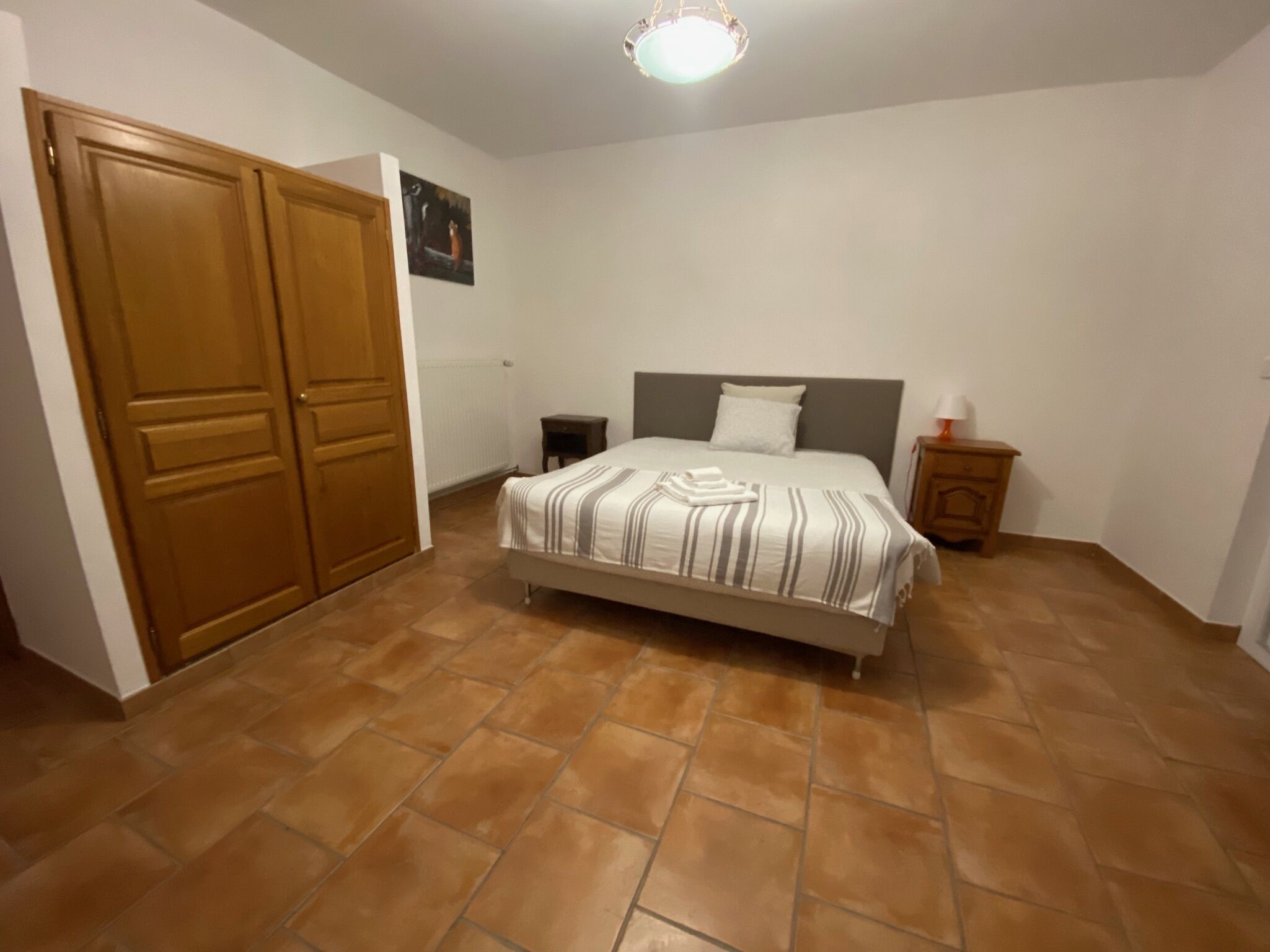 Un dormitorio con una cama, una mesita de noche, un armario de madera y una lámpara en el techo.
