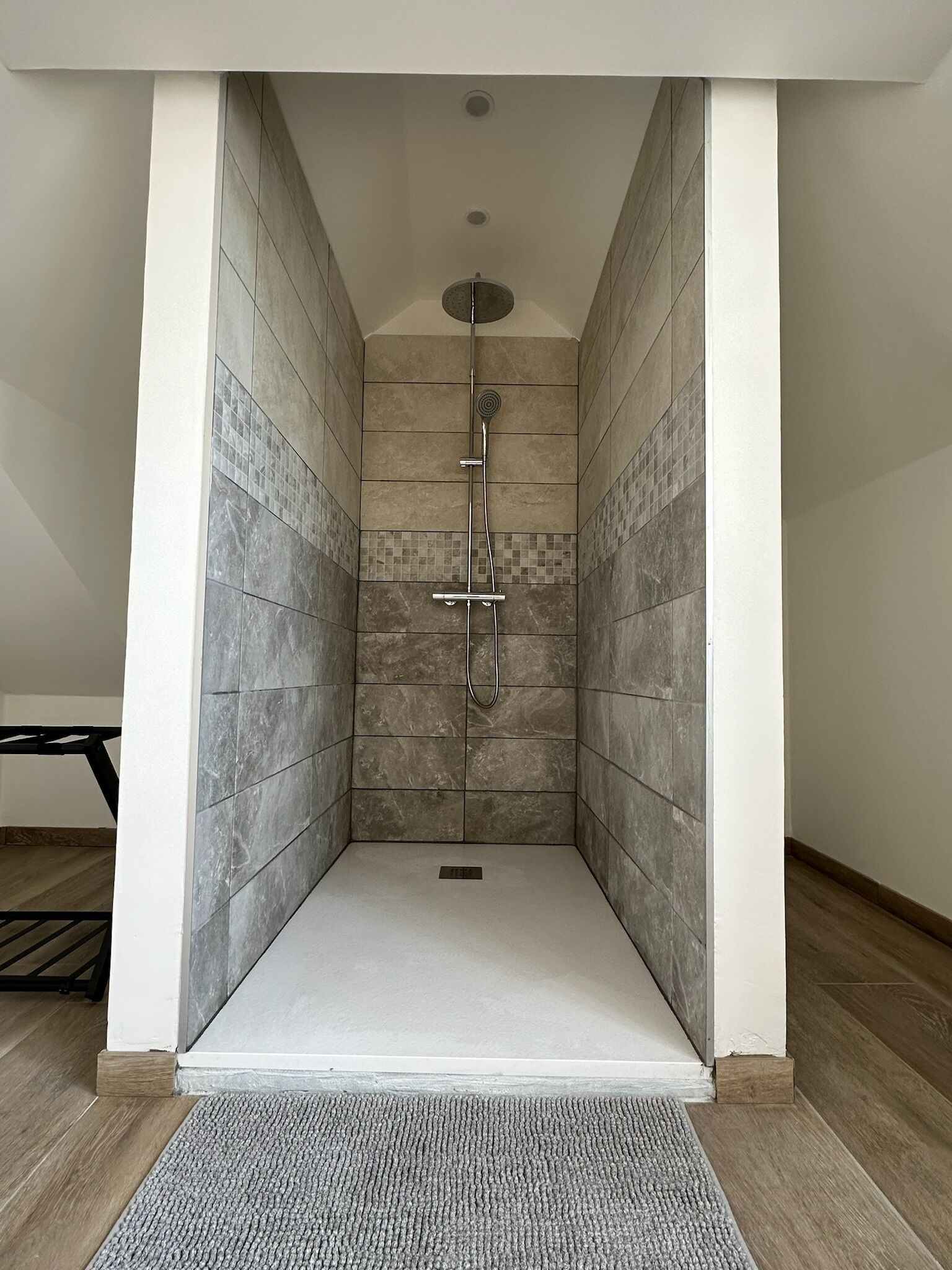 Un baño moderno con paredes y suelo de azulejos, un cabezal de ducha y una ducha de mano.