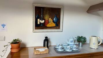 A kitchen counter with a framed painting, a kettle, a tray with teacups, and a potted plant.