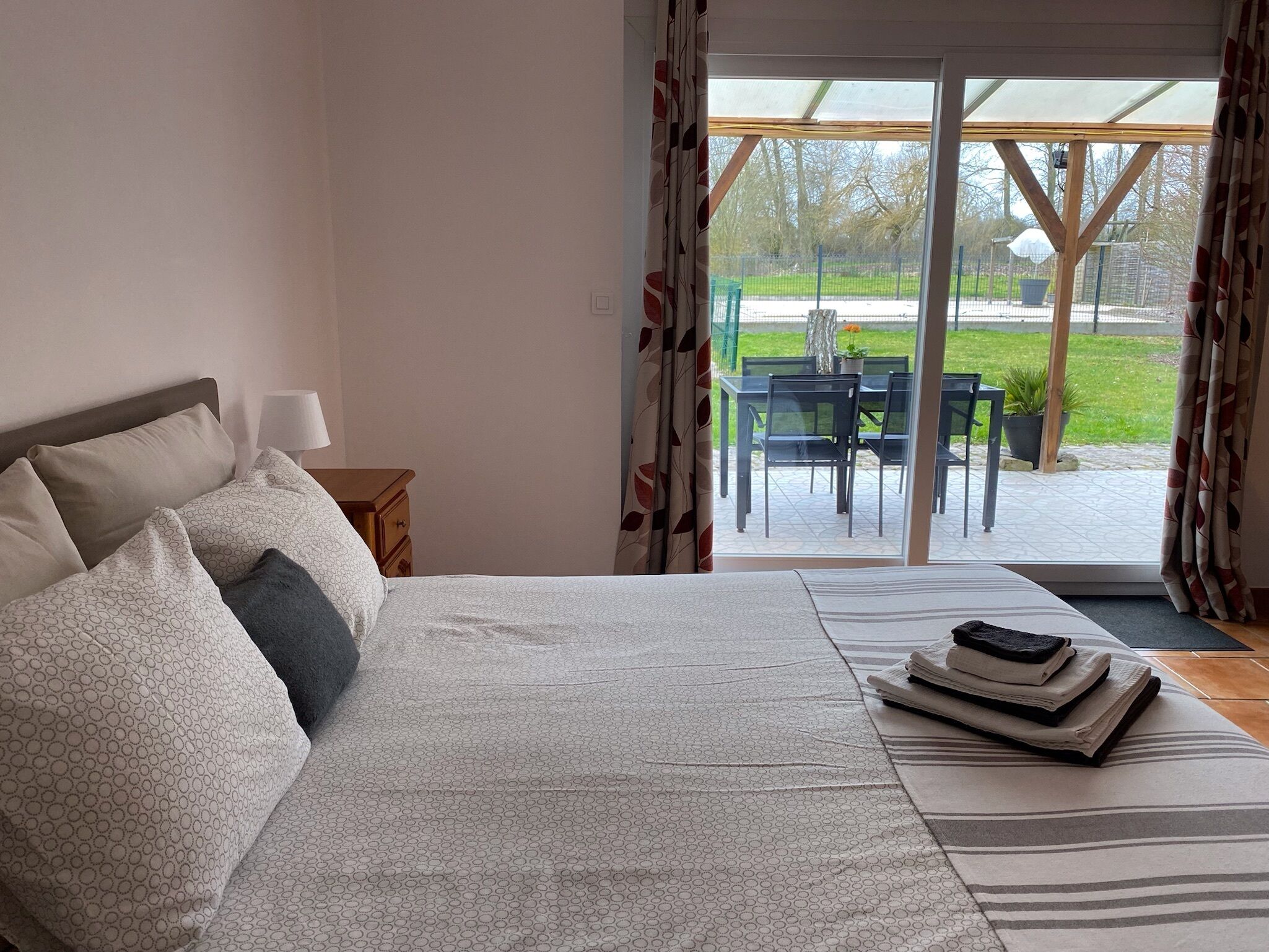 Un dormitorio con cama, mesita de noche, lámpara y vistas a un patio exterior con mesa y sillas.