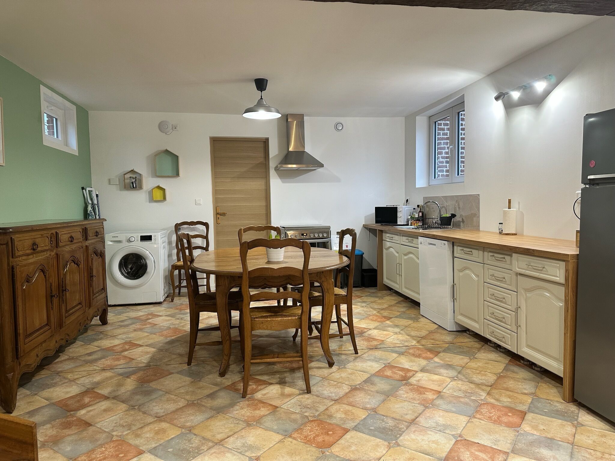 Una cocina compacta con una mesa de comedor, sillas de madera, lavadora y refrigerador.