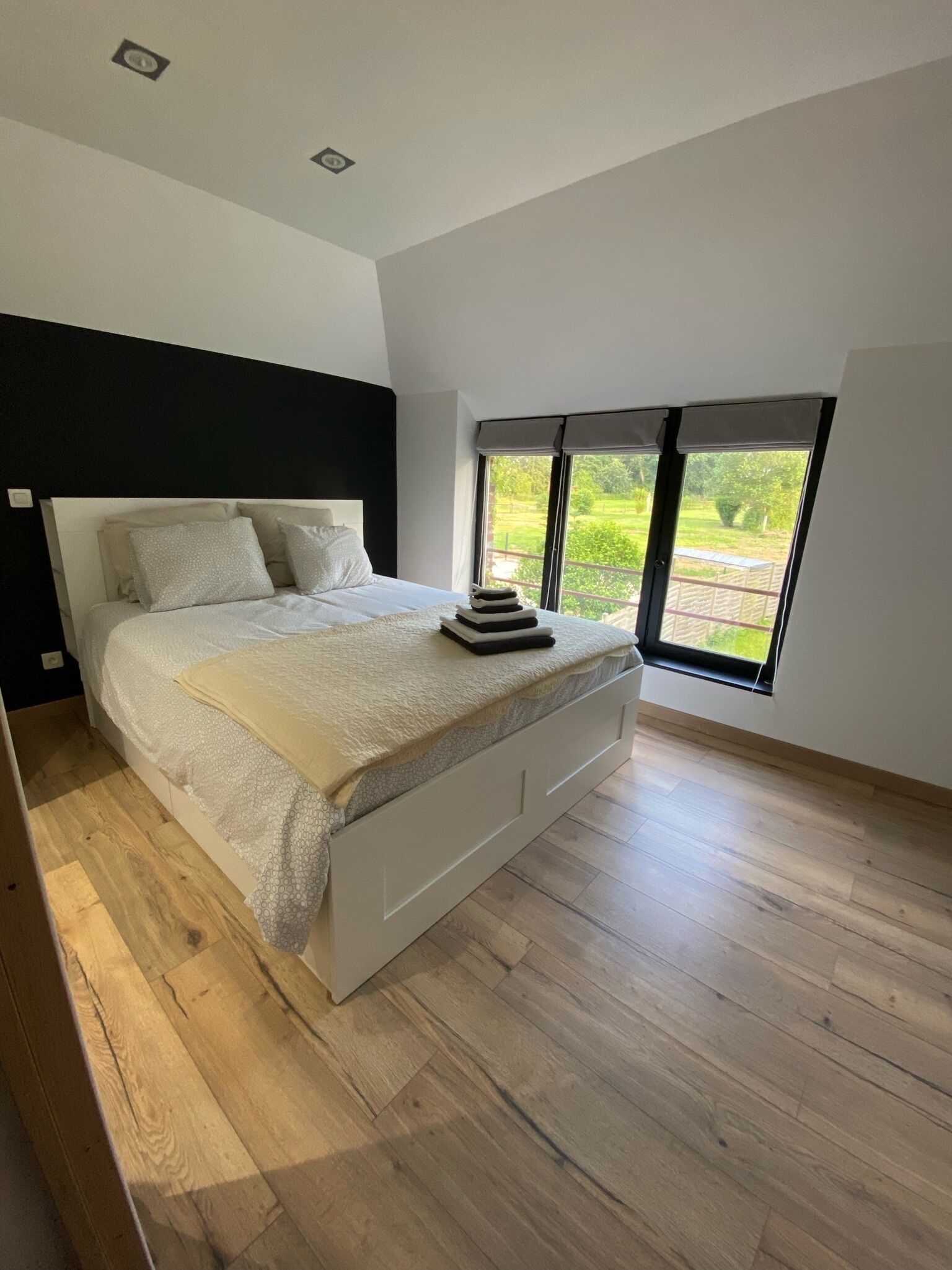A modern bedroom with a large bed, a black headboard, and a view of a garden through a large window.