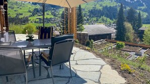 A patio with a table and chairs, a large umbrella, and a scenic mountain view. - Untere Bühlstrasse 10 - EG by Interhome (Lenk)