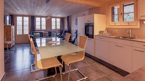 A cozy room with a wooden ceiling, a dining table with chairs, a sofa, and a kitchen area with cabinets and a sink. - Untere Bühlstrasse 10 - EG by Interhome (Lenk)