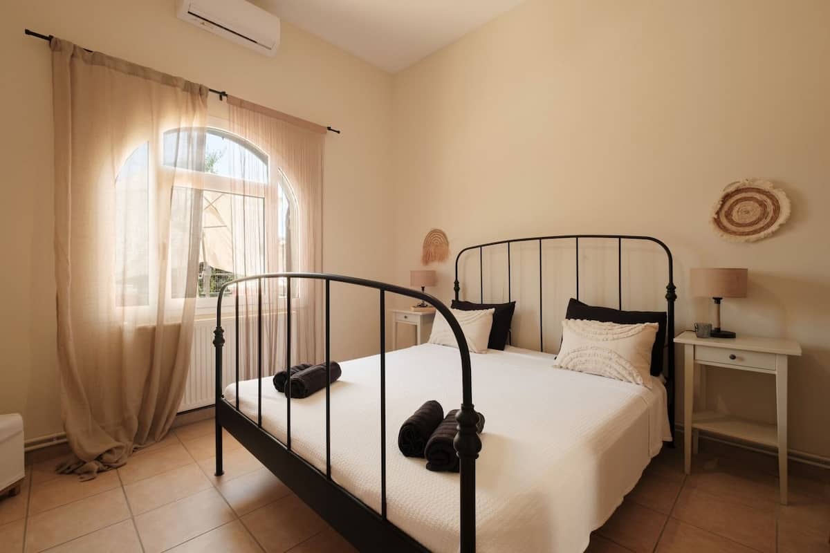 A bedroom with a bed, a bedside table, a lamp, and a window with curtains.