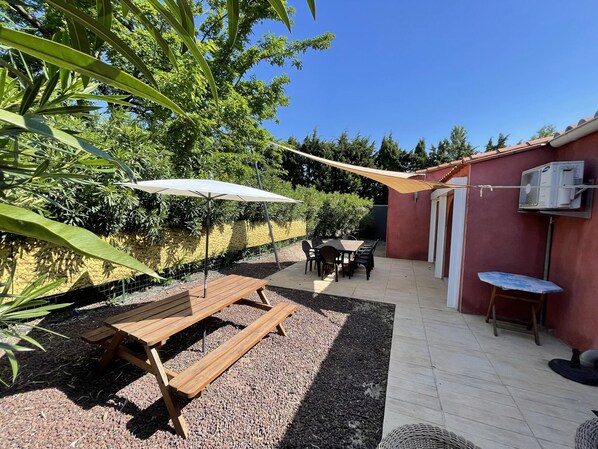 A patio area with a wooden table and benches, a white umbrella, and a red building with an air conditioning unit.