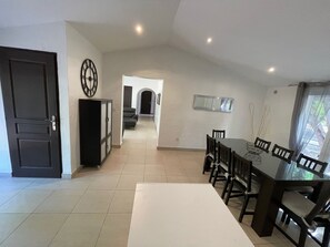 A dining area with a long table and chairs, a dark door, and a hallway leading to another room.
