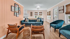 A living room with a sofa, chairs, and a coffee table. There are framed pictures on the wall and a chandelier. - Modern Tropical Bungalow, 3BR 2 Bath (Murrells Inlet)