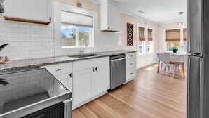 A modern kitchen with white cabinetry, a granite countertop, and a dishwasher. - Modern Tropical Bungalow, 3BR 2 Bath (Murrells Inlet)