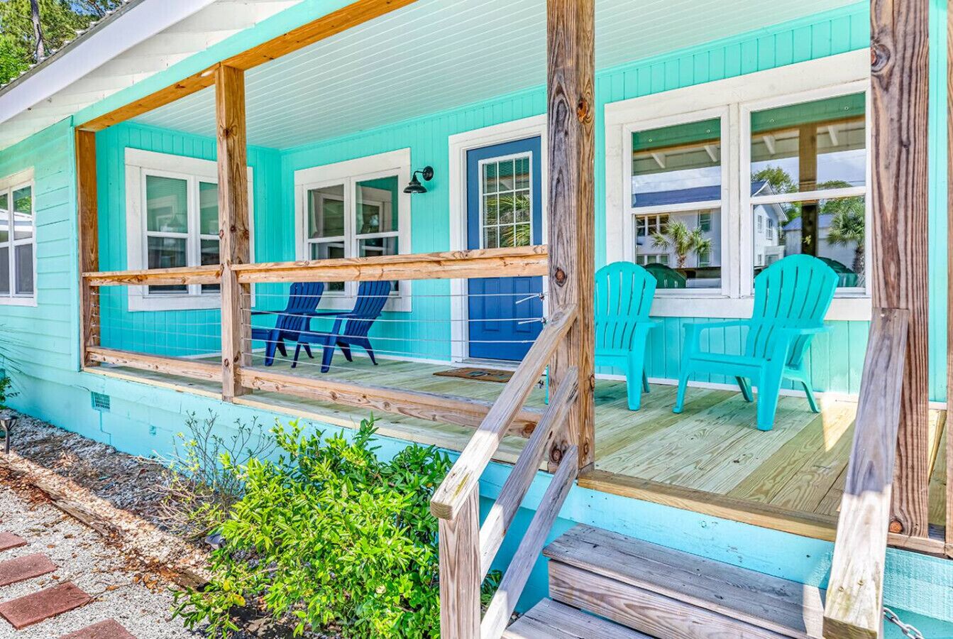 A turquoise house with a porch, blue chairs, and a wooden deck.