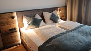 Ein ordentlich bezogenes Bett mit Holz-Kopfteil, ein Nachttisch mit Schublade und ein Fenster mit Vorhängen.